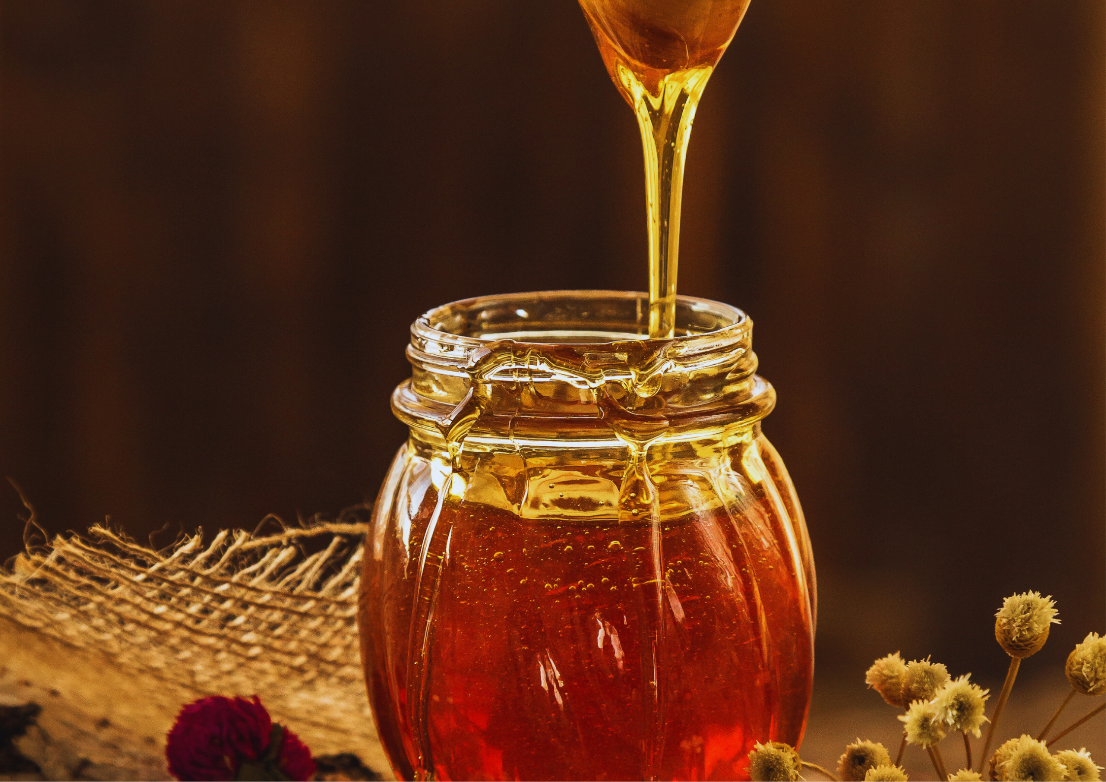 Glas mit goldfarbenem Honig, aus dem ein Löffel süß tropft.