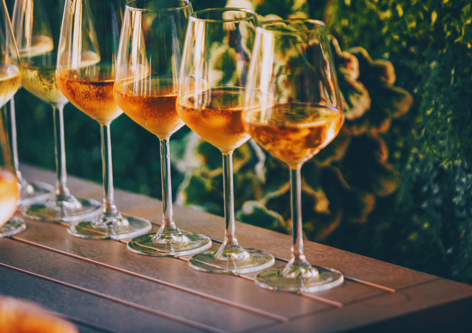 Mehrere Gläser Roséwein auf einem Tisch bei Sonnenuntergang im Grünen.