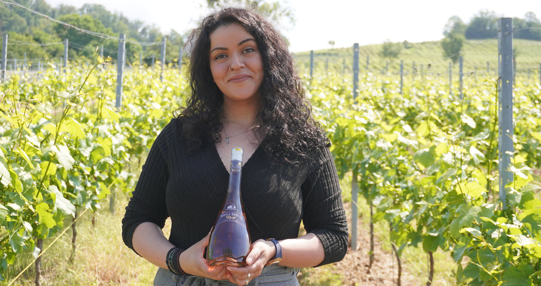 Frau steht im Weinberg und hält eine Flasche Wein in den Händen.