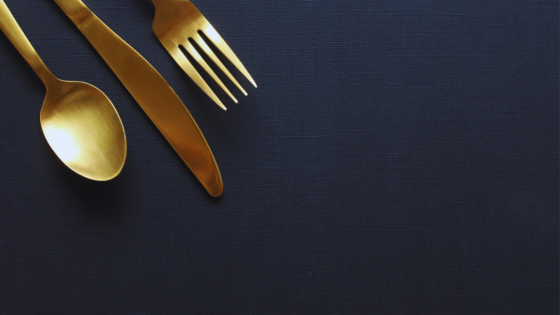 „Goldenes Besteck auf dunkelblauer Tischdecke – stilvolle Deko für feine Gastronomie“