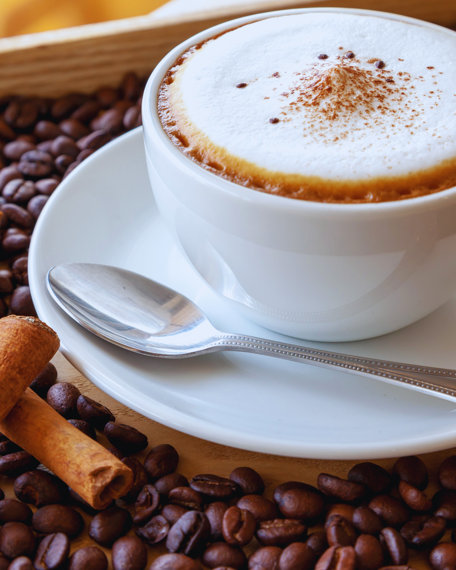 „Cappuccino mit Milchschaum und Zimt in weißer Tasse – serviert mit Bohnen und Zimtstange“