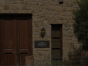 Steinfassade mit Holztor und kleinem Firmenschild neben einem schmalen Fenster.