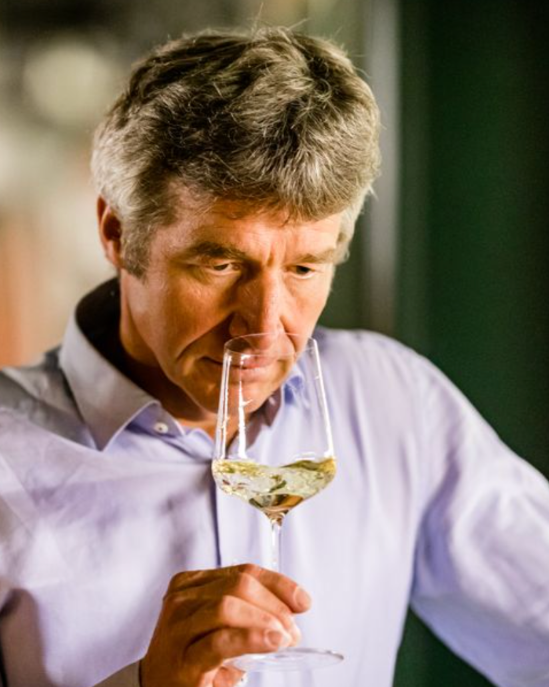 Mann riecht konzentriert an einem Glas Weißwein in heller Umgebung.