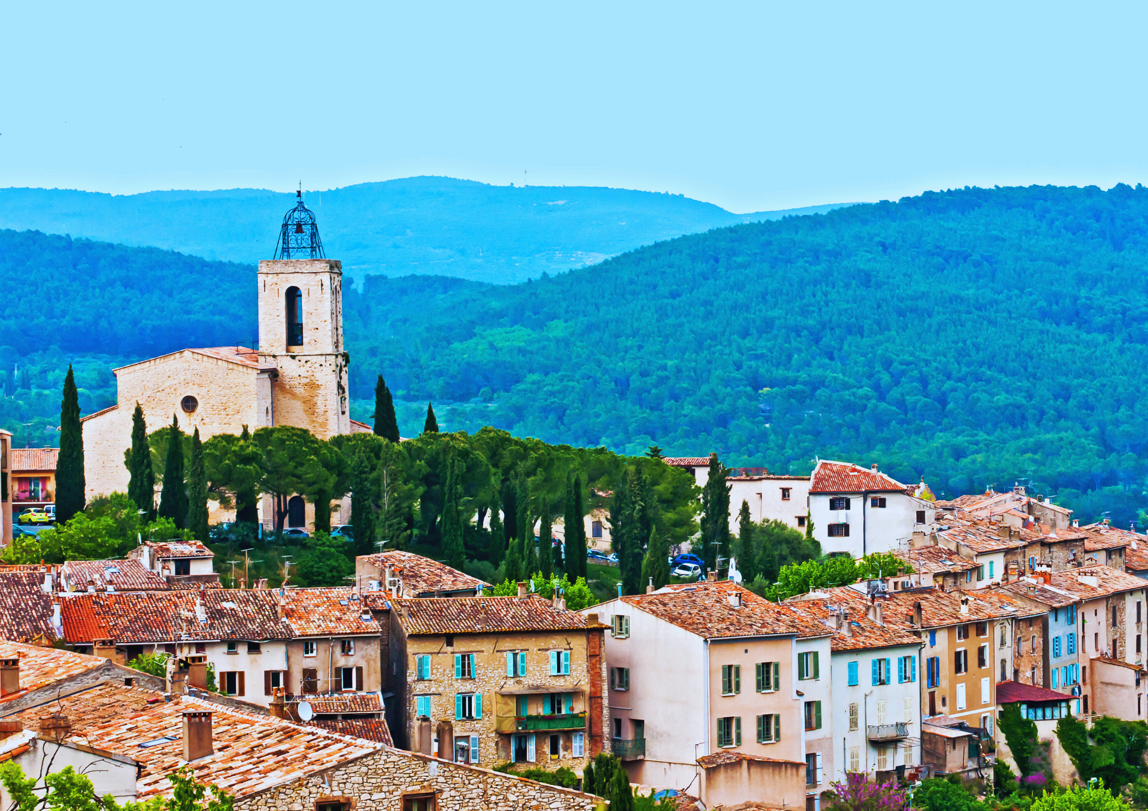 Mittelalterliches Dorf mit Kirche vor bewaldeten Hügeln in Südfrankreich.