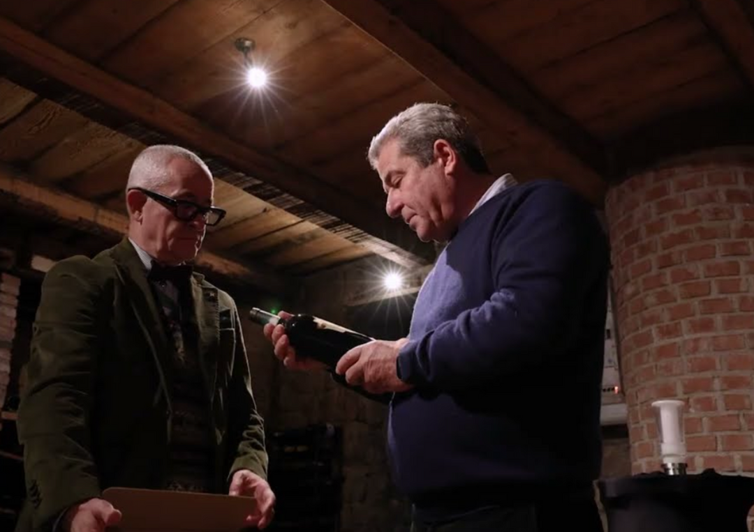 Zwei Männer betrachten gemeinsam eine Weinflasche in einem stimmungsvoll beleuchteten Weinkeller.