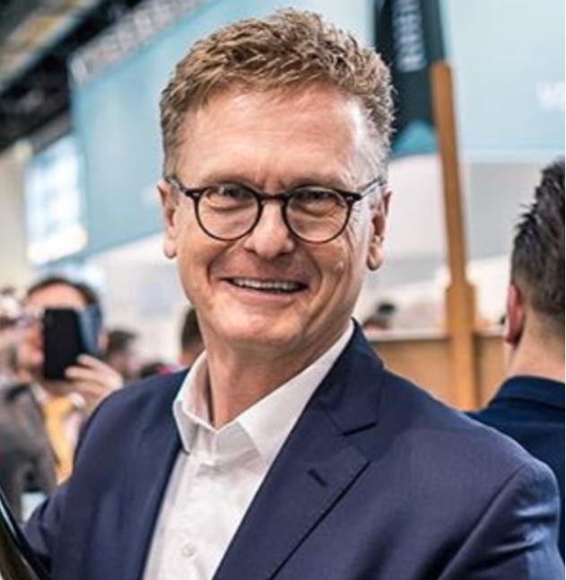 Mann auf Messe hält riesige Weinflasche von Weingut Robert Weil und lächelt in die Kamera.