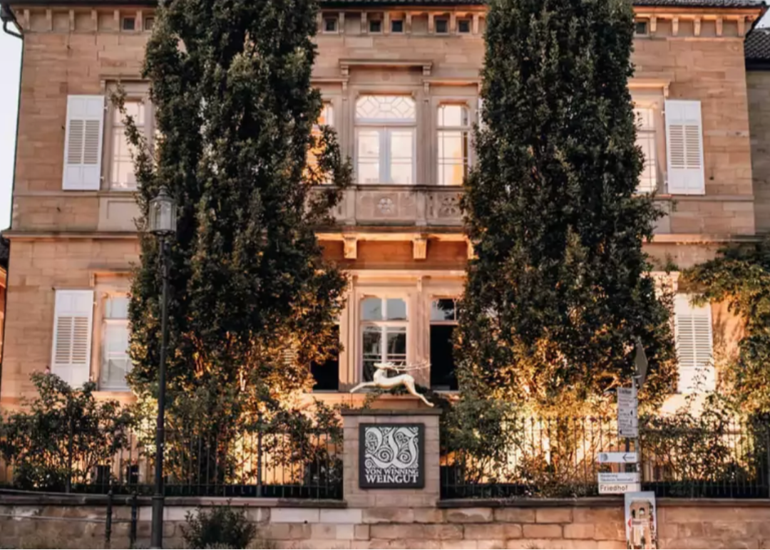 Beleuchtetes Weingut mit klassischer Fassade und hohen Zypressen am Abend.