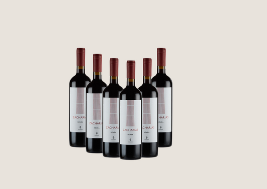 Sechs Flaschen Rotwein Zacharias Nemea mit weißem Etikett und rotem Verschluss.